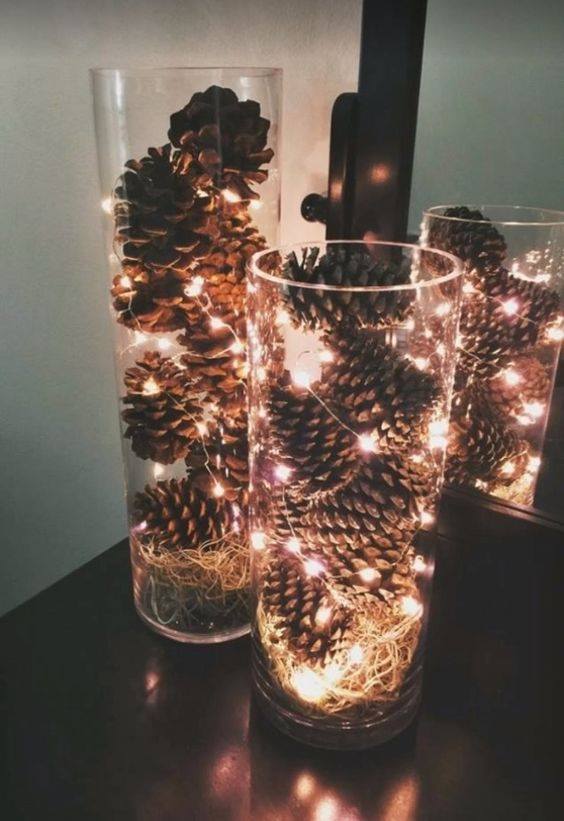 Glass Vase Is Decorated With Pine Cones And Fairy Lights