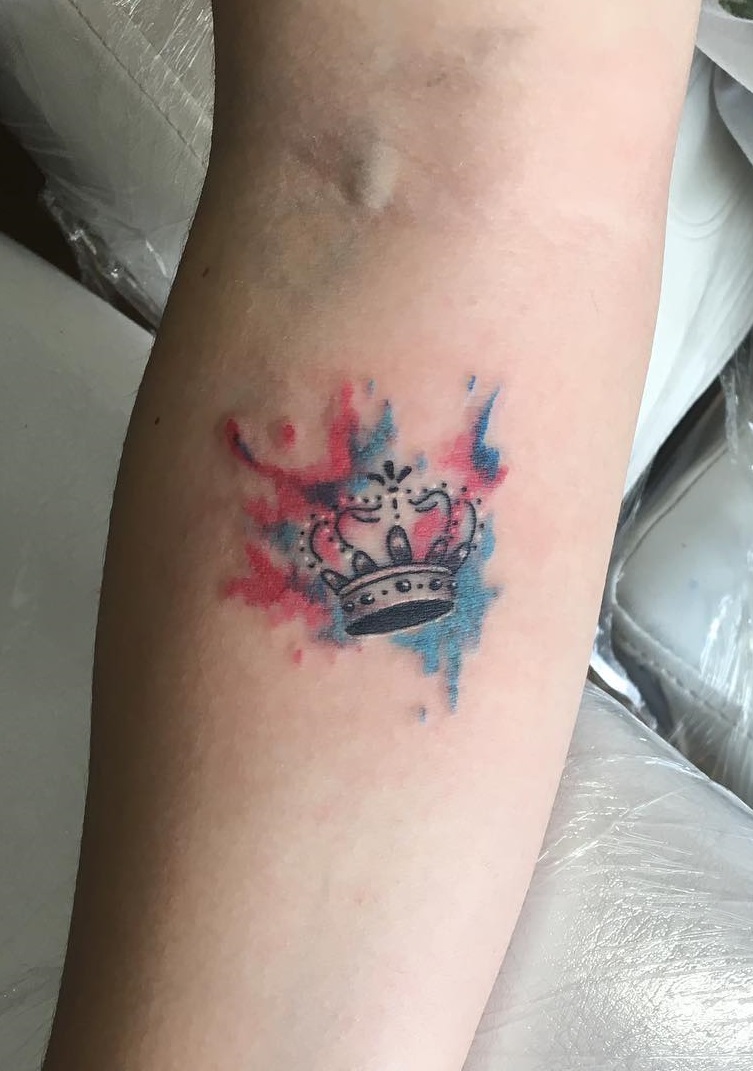 A crown is colored with blue and red water color smears on the wearer lower arm.