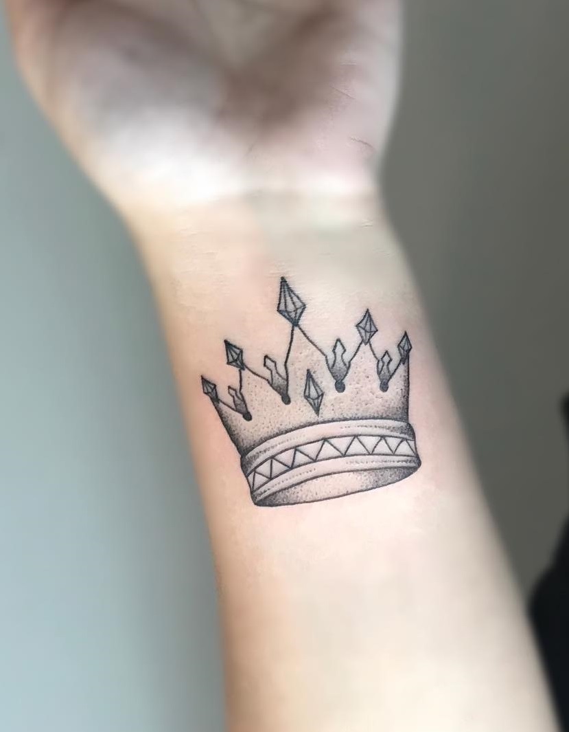 A simple black outline and dot work tattoo creates a crown on wrist.