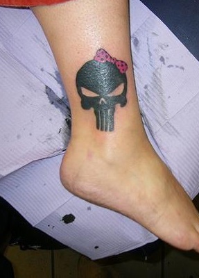 Black solid skull tattoo with pink ribbon on ankle.