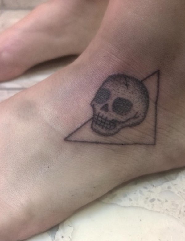 Dot work small skull tattoo with triangle on ankle.