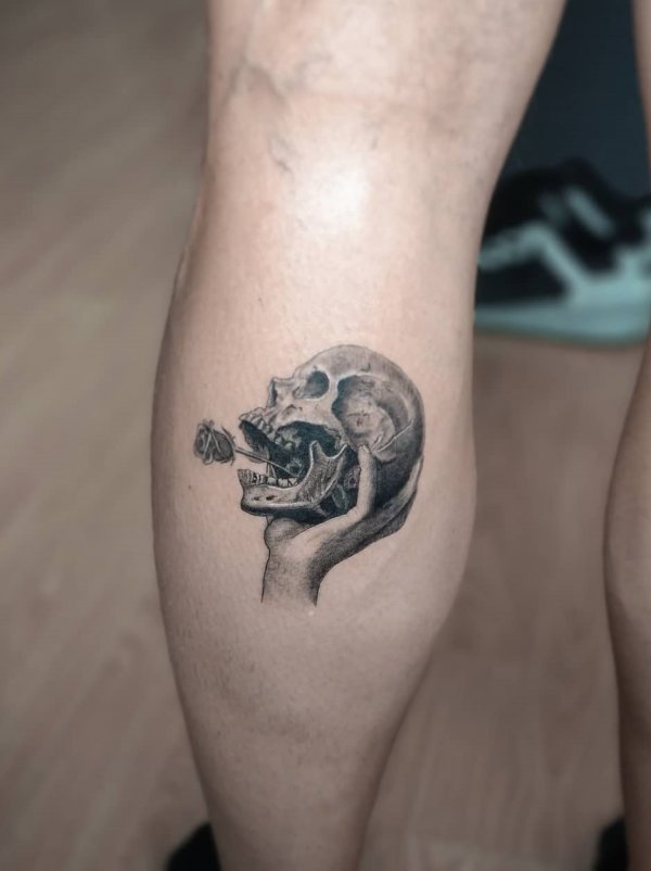 Hand holding skull inked on lower leg.