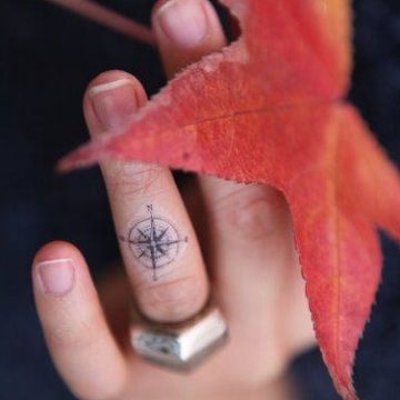 Little compass inked on ring finger.
