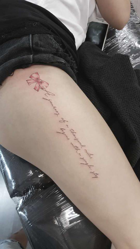 Pretty ribbon tattoo with quote on thigh.