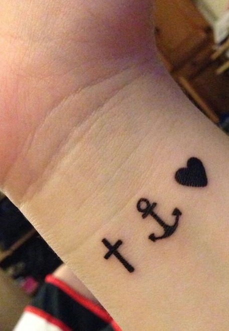 Little black tattoos of heart, anchor and cross on wrist.