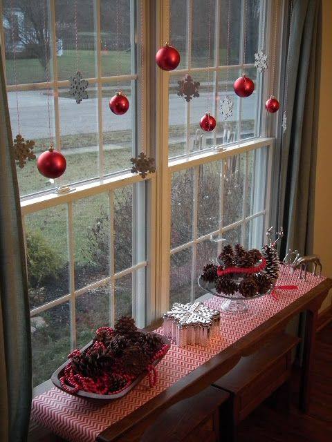 Red balls and snow hanging on windows with pinecones in a tray.