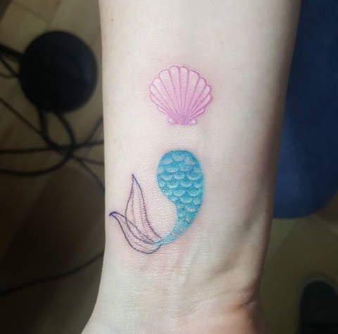 A mermaid tail and seashell disguised as semicolon wrist tattoo.