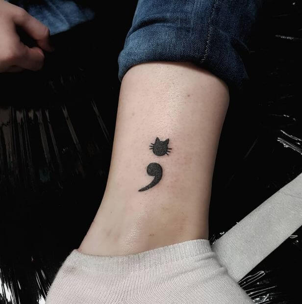 An ankle tattoo of semicolon with cat face.