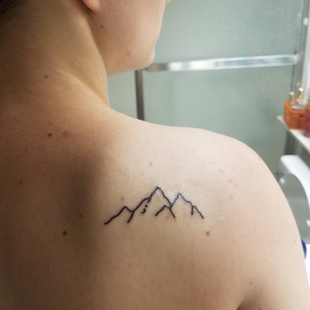 Fineline mountain semicolon tattoo on back shoulder.