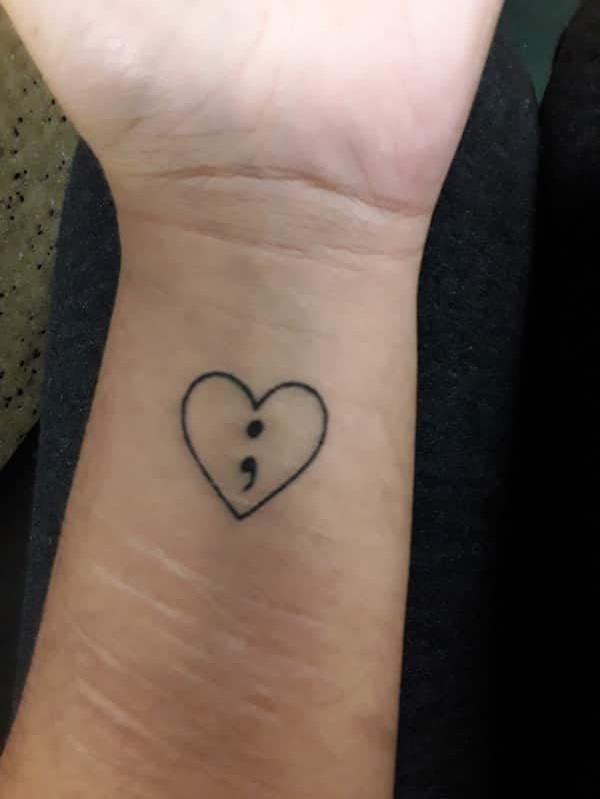 Sassy wrist tattoo of a heart with the semicolon punctuation mark in the middle.