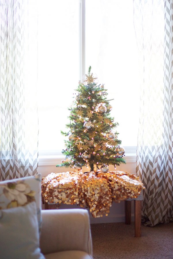 Little tree decorated with sparkly ornaments, a gold tree skirt, and a string of lights.
