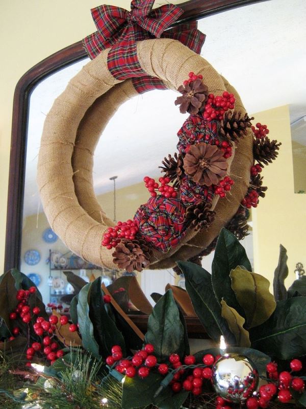 Burlap wreath decorated with plaid flowers and berries.