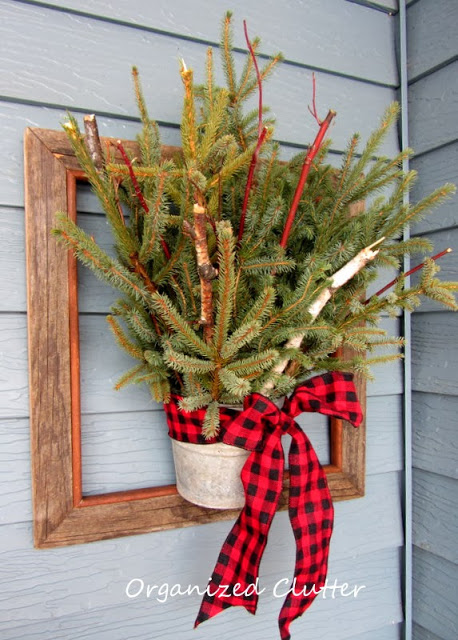 Wooden frame is decorated with Christmas tree and plaid bow.